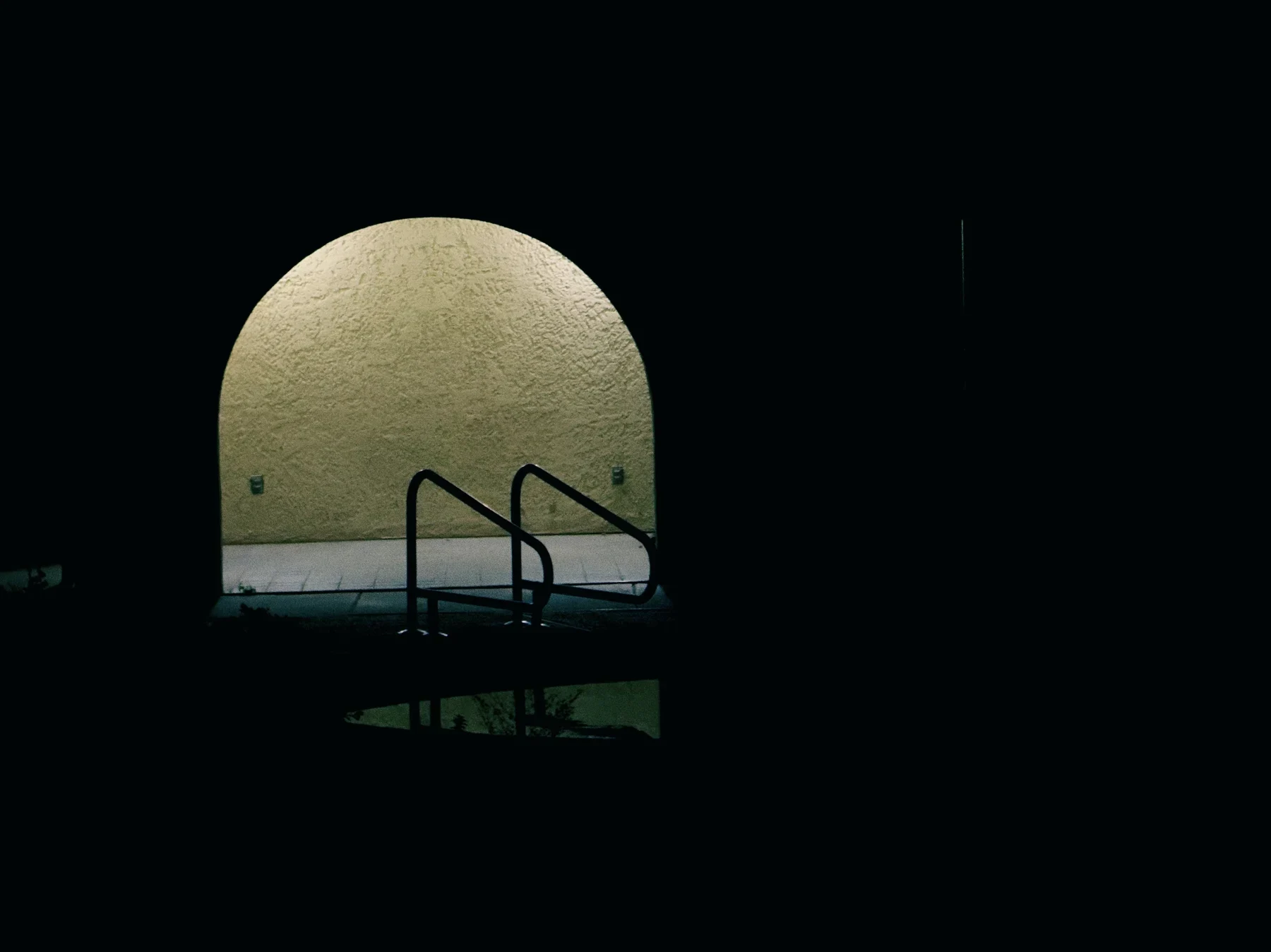 Pool ladder beneath an illuminated arch at night