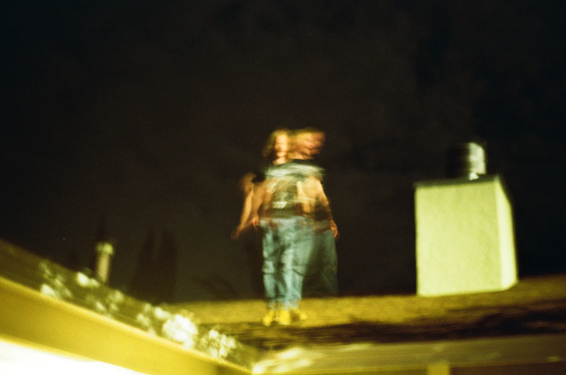 A figure in green standing on a lit rooftop at night